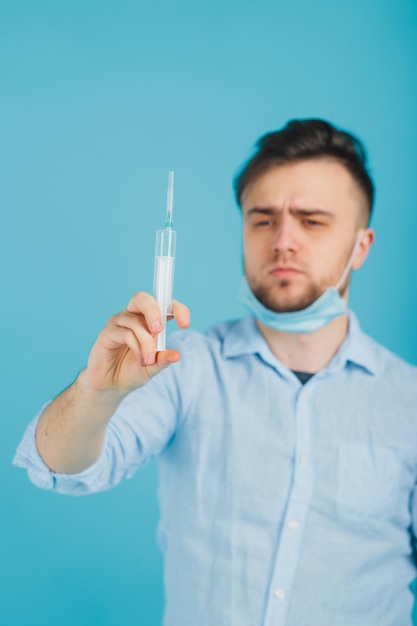 médico masculino barbudo e segurando a seringa e gritando sobre fundo azul