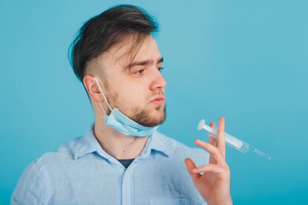 médico masculino barbudo e segurando a seringa e gritando sobre fundo azul