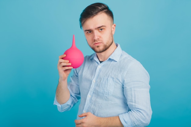 médico masculino barbudo segurando enema nas mãos sobre fundo azul