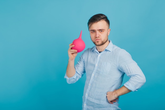 médico masculino barbudo segurando enema nas mãos sobre fundo azul