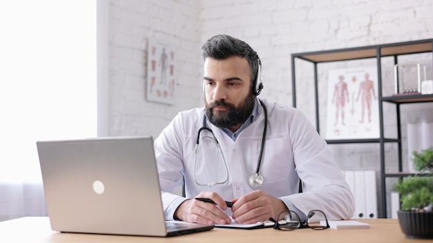 Foto el médico masculino con bata blanca tiene videollamadas, videollamadas, conferencias con colegas o pacientes.