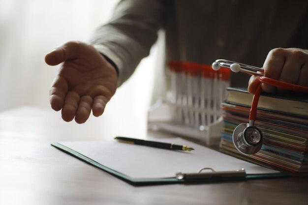 Médico masculino busca información en el libro y escribe un estetoscopio médico recetado en el escritorio de la clínica Conocimiento médico y concepto de educación