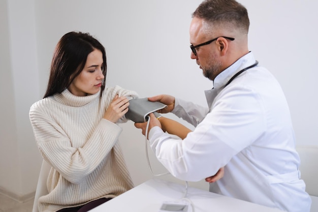 Médico masculino coloca no braço da paciente do sexo feminino o manguito do monitor de pressão arterial