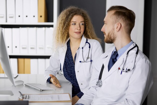 Médico masculino com colega discutindo a terapia da doença atual enquanto está sentado no local de trabalho na clínica. Trabalho em equipe na medicina.