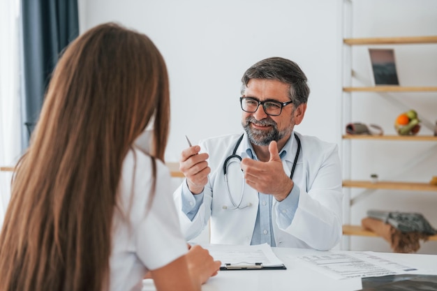 Foto médico masculino dando consulta a la mujer trabajador médico profesional en bata blanca está en la oficina