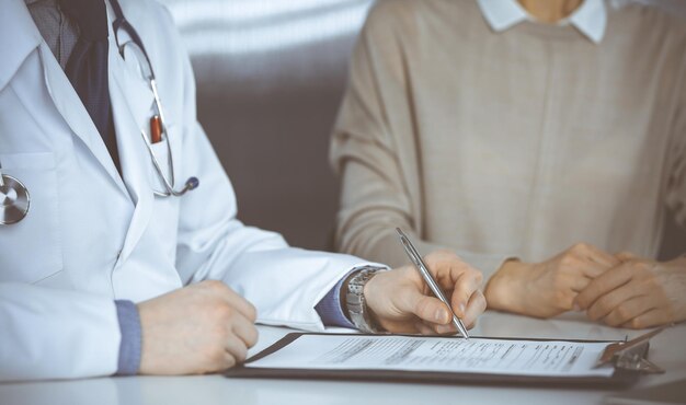 Médico masculino desconhecido e mulher paciente discutindo algo enquanto está sentado na clínica e usando a área de transferência. Melhor serviço médico em hospital, medicina, parada pandêmica.