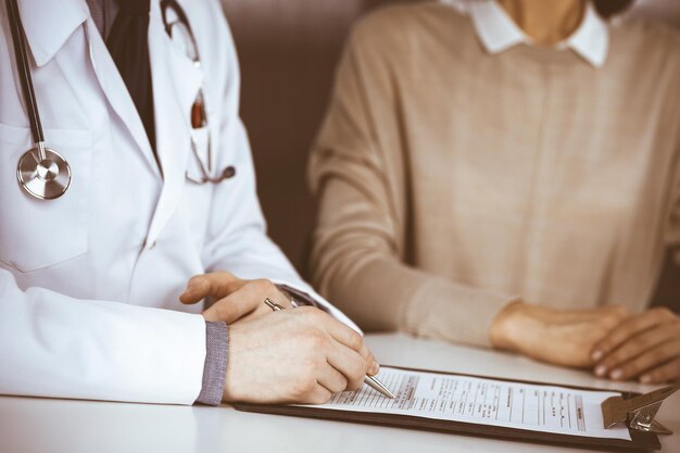 Médico masculino desconhecido e mulher paciente discutindo algo enquanto está sentado na clínica e usando a área de transferência. Melhor serviço médico no hospital, medicina, parada pandêmica