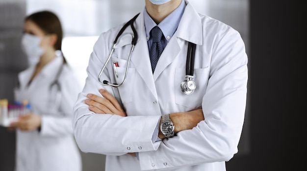 Médico masculino desconocido con máscara protectora de pie con los brazos cruzados en la clínica. Concepto de medicina durante la pandemia de Coronavirus. covid 2019.