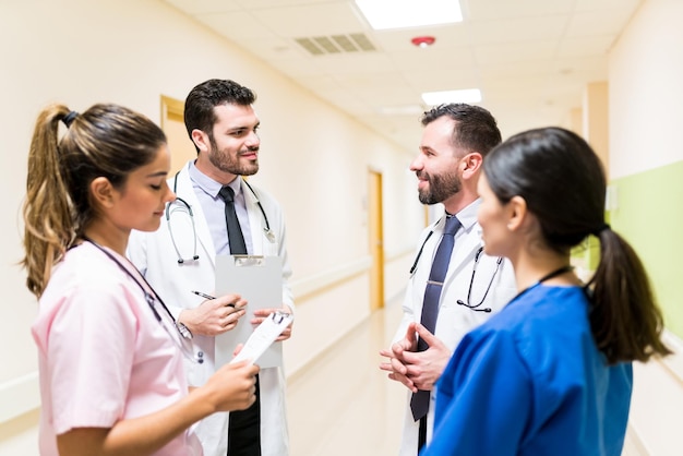 Médico masculino discutindo sobre relatórios médicos com colegas em pé no corredor do hospital