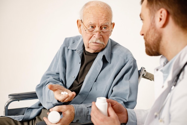 Médico masculino e ancião em cadeira de rodas isolado em um fundo branco