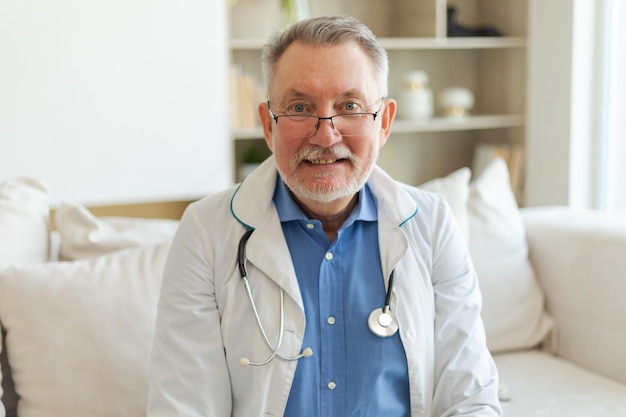 Médico masculino de edad avanzada con gafas, uniforme médico, sonriendo mirando a la cámara en el hospital general.