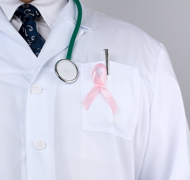 Médico masculino em um casaco branco e gravata fica e segura uma fita de seda rosa em forma de um laço
