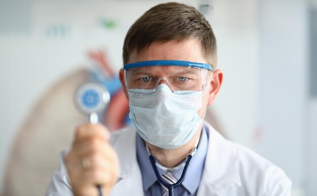 Foto médico masculino con un estetoscopio en la mano con el símbolo del coronavirus en primer plano