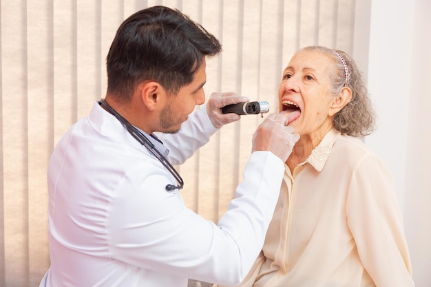 Médico masculino examinando a garganta da mulher idosa em consulta. Médico verificando a garganta da velha