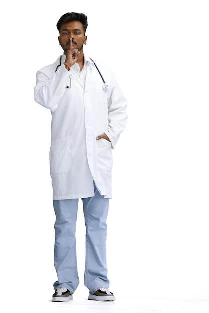 Un médico masculino en un fondo blanco a toda altura muestra un signo de silencio