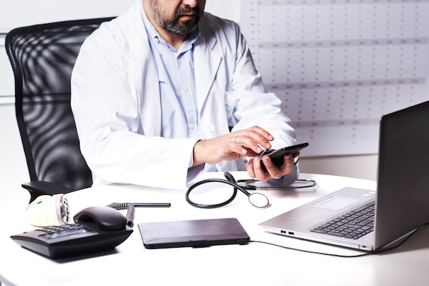 Médico masculino irreconhecível usando smartphone olhando para o celular enquanto trabalhava