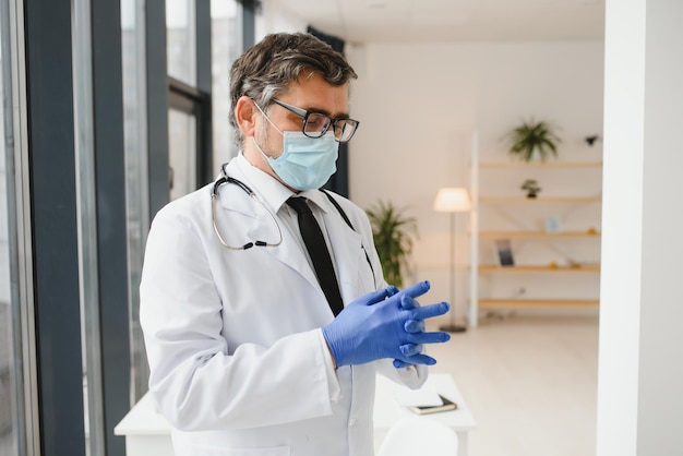 Médico masculino con una máscara protectora se pone guantes en la clínica