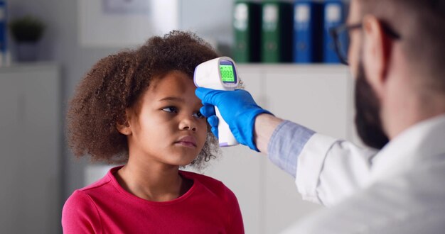 Médico masculino medindo a temperatura da criança usando termômetro eletrônico