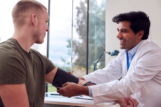 Médico masculino o médico de cabecera que examina a un paciente joven que toma la presión arterial con un esfigmomanómetro