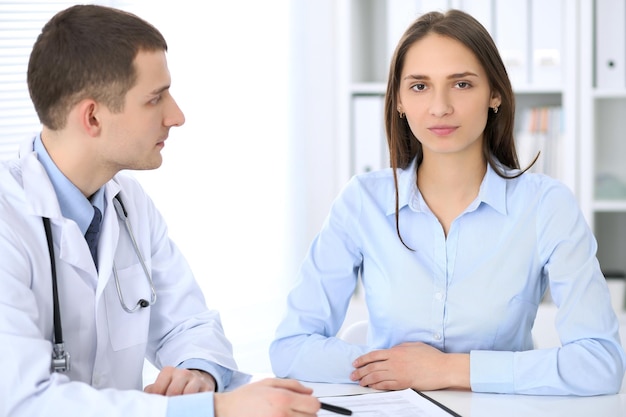 Médico masculino y paciente femenino sentados a la mesa en el gabinete médico. Concepto de servicio médico de alto nivel y calidad.