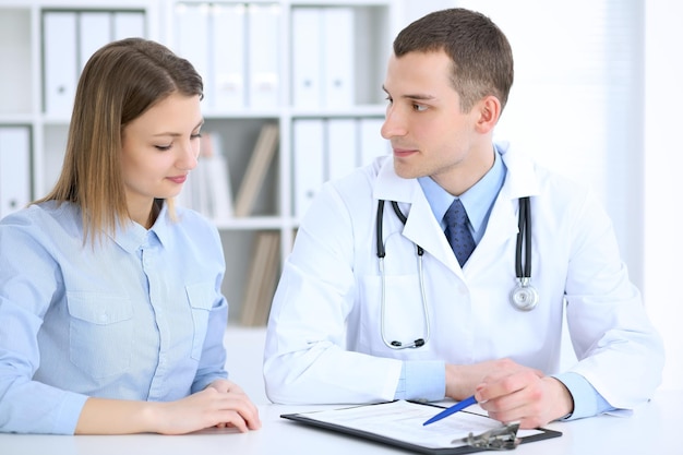 Médico masculino y paciente femenino sentados a la mesa en el gabinete médico