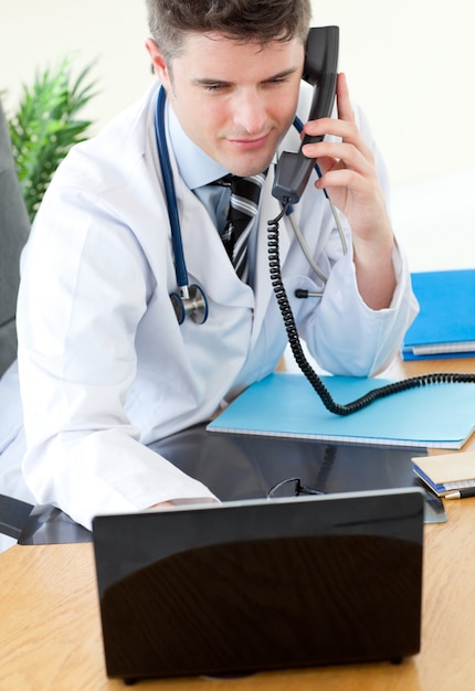 Médico masculino positivo no telefone usando seu laptop