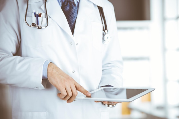 Médico masculino que usa una tableta en la clínica, primer plano. Perfecto servicio médico en el hospital. Concepto de medicina y salud.