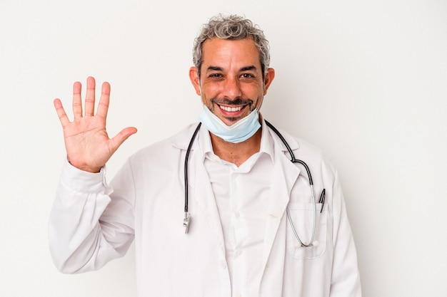 Médico de mediana edad hombre con una máscara para virus aislado sobre fondo blanco sonriendo alegre mostrando el número cinco con los dedos.