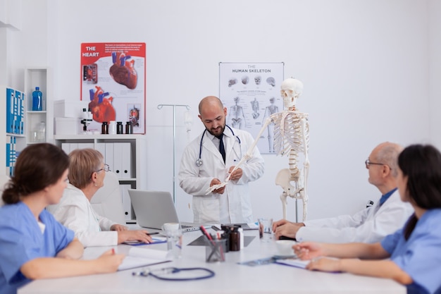 Médico médico con estetoscopio discutiendo la estructura ósea utilizando esqueleto humano analizando el cuerpo de la anatomía trabajando en experiencia médica en la sala de reuniones de conferencias