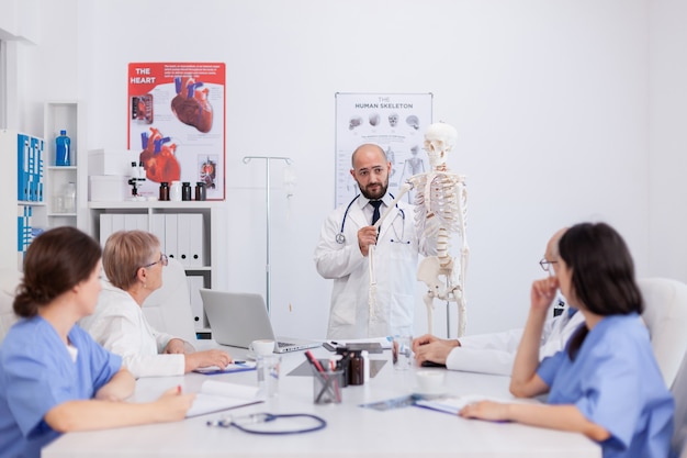 Médico médico con estetoscopio sosteniendo el hueso de la mano explicando el esqueleto humano del cuerpo que presenta la estructura de la anatomía discutiendo la experiencia médica. Equipo del hospital que trabaja en la sala de reuniones de conferencias