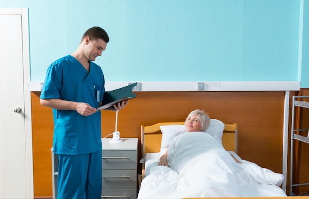 El médico mira las puntuaciones de análisis de su paciente, que está acostada en la cama del hospital en la sala del hospital. Concepto de salud