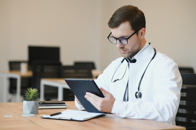 El médico moderno Captura recortada de un apuesto médico que trabaja en su tableta mientras está sentado en su oficina