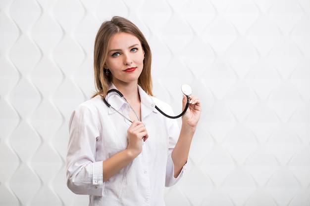 Médico mostrando como usar um estetoscópio vestindo médicos smock menina caucasiana de cabelos louros isolada