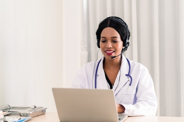 Médico de la mujer africana en auriculares tomando llamada en su micrófono auricular en línea para un paciente con dolor