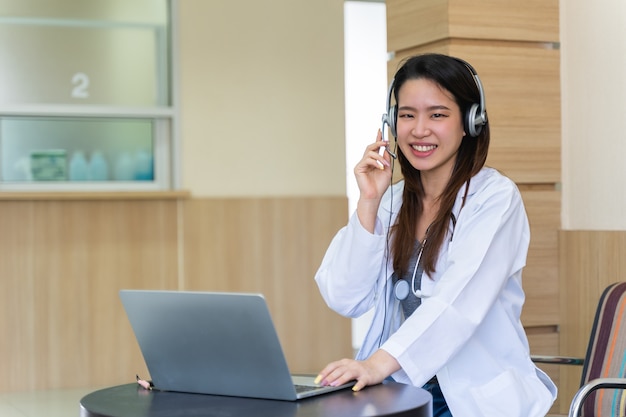 Médico de la mujer asiática en auriculares tomando llamada en su micrófono de auriculares en línea para un paciente con dolor