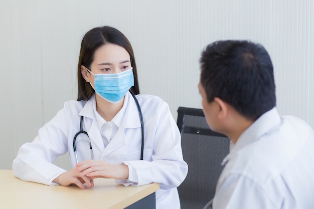 Médico mujer asiática Hacer preguntas a los pacientes Llevando una mascarilla quirúrgica en todo momento