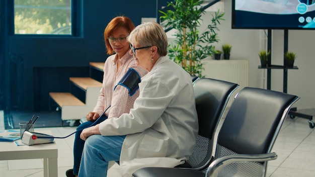 Médico y mujer asiática usando tonómetro para medir la hipertensión, controlando la presión arterial alta o baja en el chequeo en el vestíbulo de espera. Haciendo cita de examen médico en el centro de salud.