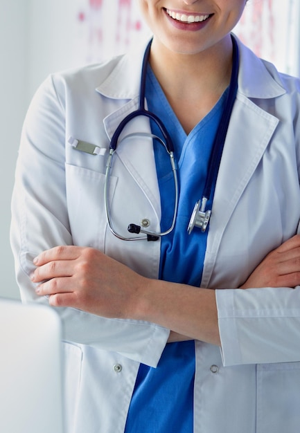 Médico de mujer joven en uniforme blanco de pie en la oficina de clínicas