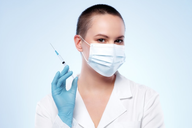 Médico de la mujer de pelo corto en máscara con jeringa con medicación