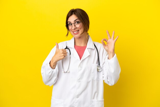 Médico mulher isolada em fundo amarelo mostrando sinal de ok e polegar para cima gesto