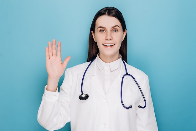 Médico mulher vestindo uniforme médico acenando e dizendo olá feliz e sorrindo