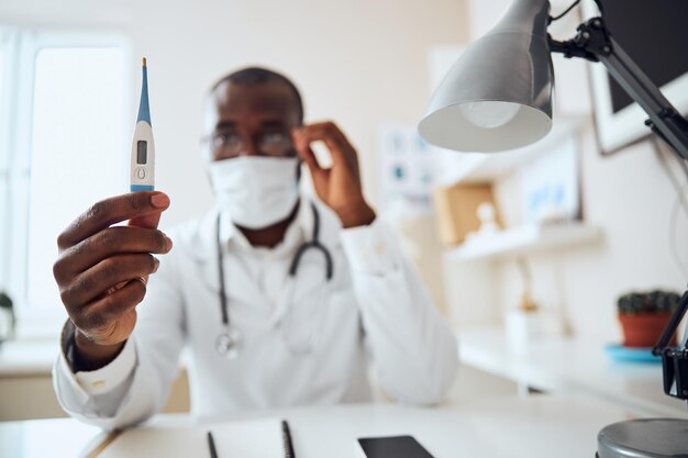 Médico multirracial tomando las lecturas de un termómetro