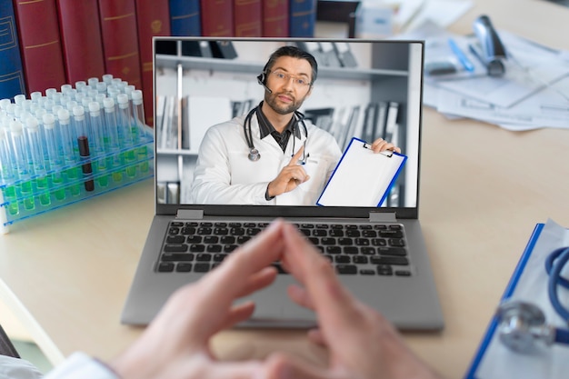 Foto médico na frente de um monitor de laptop durante uma conversa por videochamada online com um colega