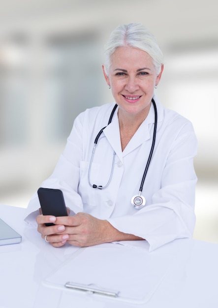 Médico na mesa com telefone contra janelas desfocadas brancas