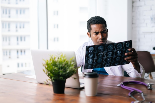 Médico negro afro-americano está analisando a varredura da cabeça do cérebro de ressonância magnética e trabalhando no laptop