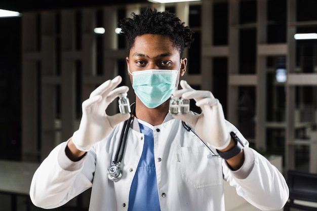 Médico negro com 3 doses de vacina Vacinação de reforço Médico africano com máscara médica está segurando vacinas na mão