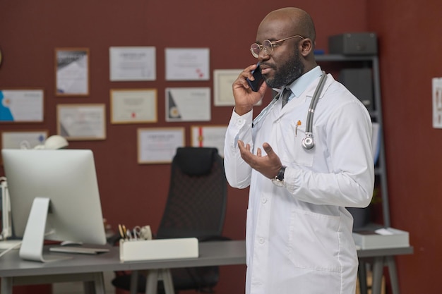 Médico negro falando por telefone móvel na clínica