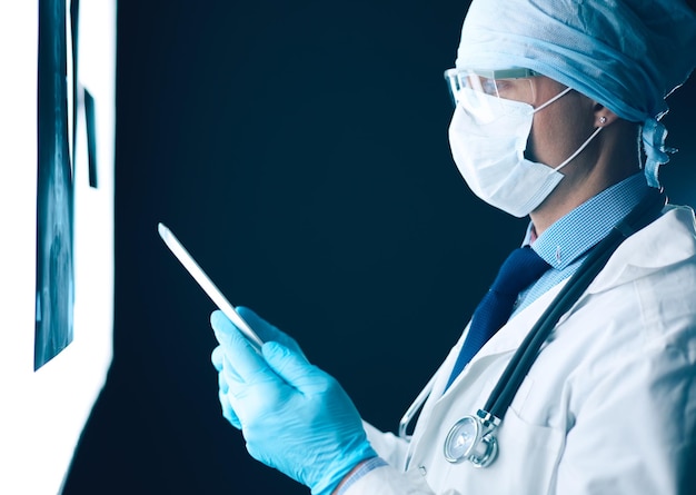 Médico no hospital sentado na mesa olhando raios-x no tablet contra fundo branco com raios-x