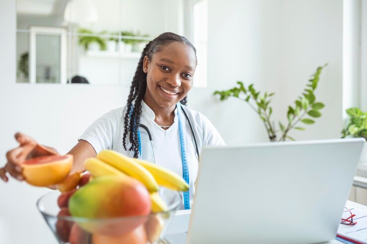 Médico nutricionista com frutas no escritório Nutricionista trabalhando no laptop e escrevendo um plano de dieta para o paciente Retrato de uma nutricionista em seu escritório Sorrindo jovem nutricionista sentado na mesa