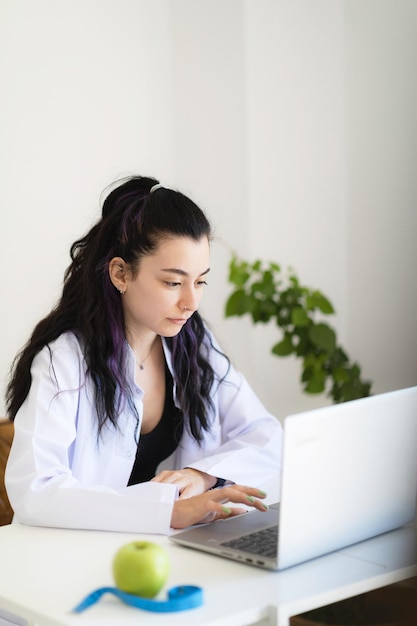 Médico nutricionista sentado em seu gabinete na clínica de perda de peso usando laptop dando consulta on-line sobre alimentação saudável e programa de plano de refeições